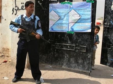 A schoolboy peers from behind a gate as an Iraqi policeman stands guard outside a school that will serve as voting station in Baghdad, Iraq, Tuesday, Oct. 11 2005.